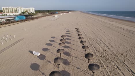 Drone-Volando-Hacia-Atrás-Sobre-La-Playa-De-Montegordo,-Sombreros-Para-El-Sol-Del-Resort-De-Playa,-Algarve