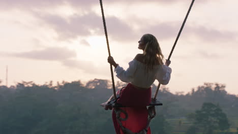 happy woman swinging over tropical rainforest at sunrise sitting on swing with scenic view enjoying freedom on vacation having fun holiday lifestyle slow motion