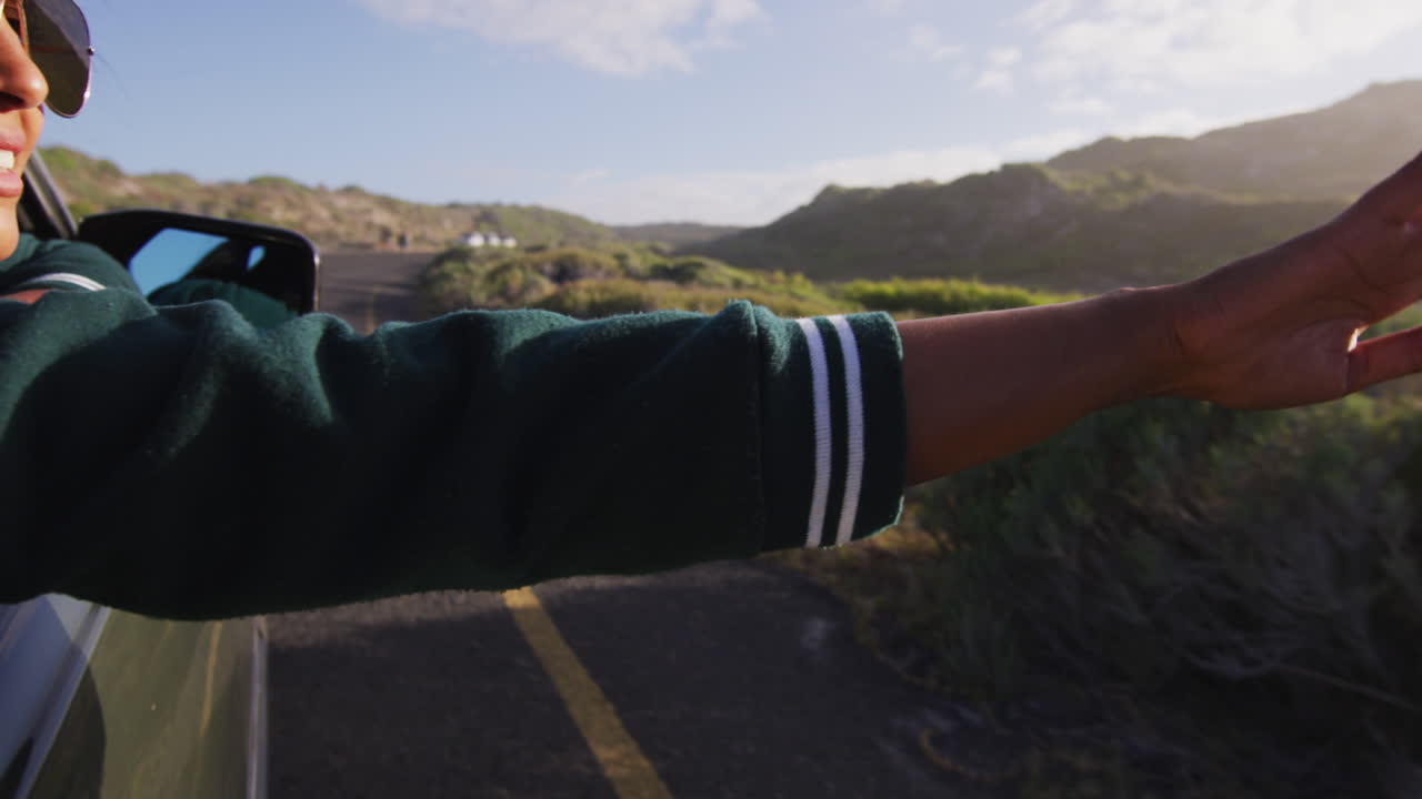 혼성 인종의 여성이  ⁇ 은 날 카브리톨 자동차를 운전하며 팔을 흔들고 미소 짓고 있습니다.