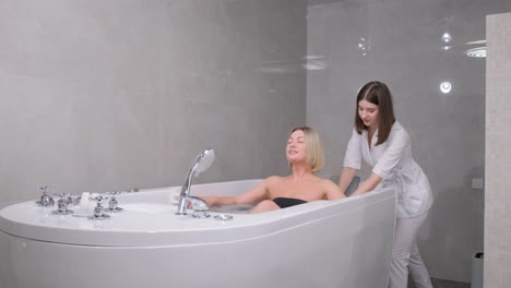 relaxed, beautiful woman lying in a hot tub in a spa salon. a beautician gives a health massage to a client.