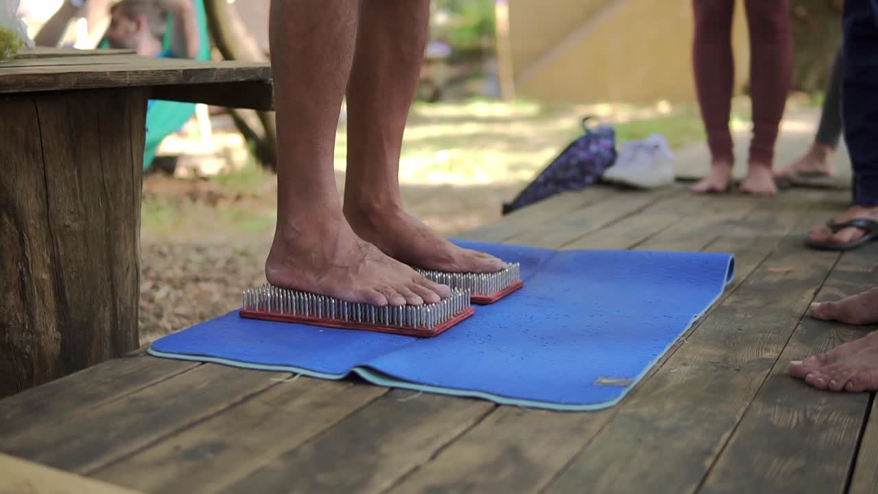 pies masculinos paso en una tabla de yoga de madera con un montón de clavos de metal alfileres alrededor de diversas personas irreconocibles