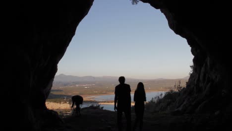 Silhouettes-of-people-in-the-entrance-of-Nestor's-cave-with-the-lake-of-Gioalova-in-the-background-in-Greece