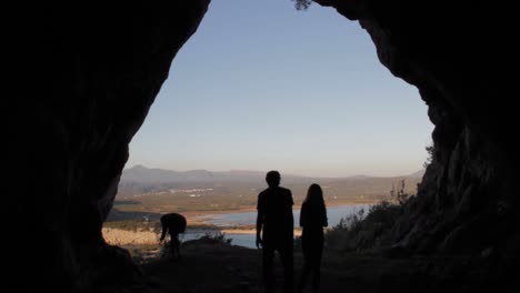 siluetas de personas en la entrada de la cueva de nestor con el lago de gioalova al fondo en grecia