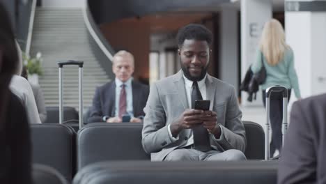 smiling afro-american man using smartphone in busy departure lounge