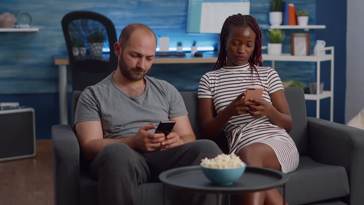 Interracial couple looking at smartphones in living room