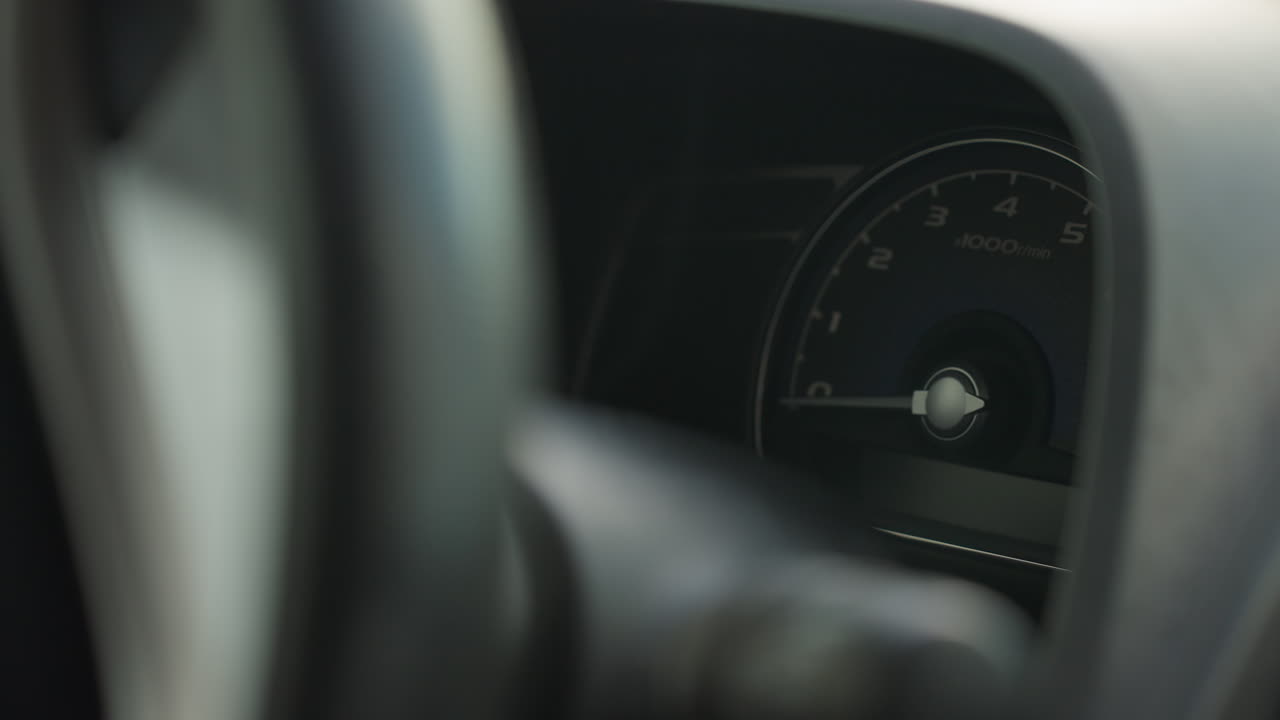 close up of car dashboard gear indicator with needle shifting position as car powers on, showing mechanical movement behind steering wheel under soft lighting and blurred background