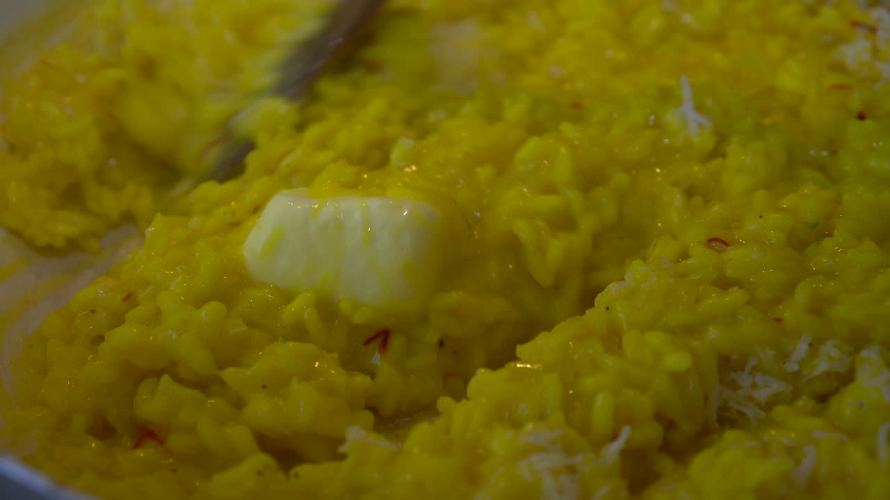Mescolando cremoso risotto allo zafferano giallo con un pezzo di burro che si scioglie al centro