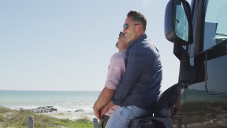 Feliz-Pareja-De-Hombres-Gay-Caucásicos-Con-Gafas-De-Sol-Abrazándose,-Apoyado-En-El-Coche-En-Un-Día-Soleado-Junto-Al-Mar