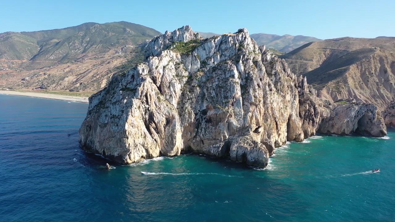 Ampia prospettiva aerea che mostra una monumentale scogliera marina di calcare bianco che si erge drammaticamente sopra acque blu profonde lungo la costa mediterranea marocchina