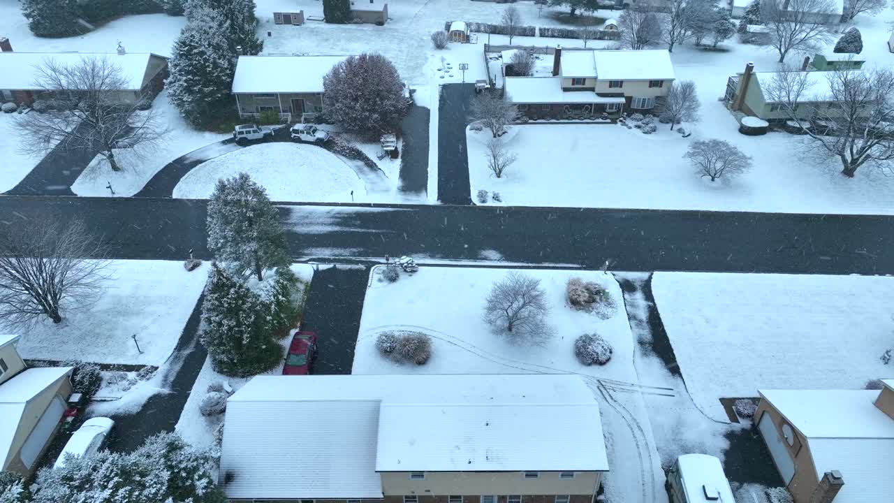 vista de invierno de un barrio suburbano con casas cubiertas de nieve, patios y carreteras, bajo un cielo gris
