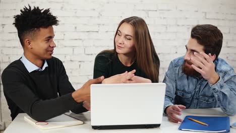 grupo diverso de jóvenes empresarios discutiendo mientras están sentados alrededor de una computadora portátil blanca. están discutiendo un proyecto de negocio en la oficina