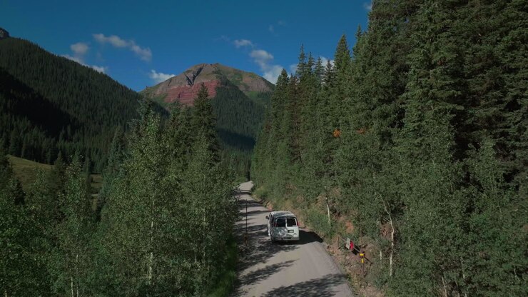 Aerial drone cinematic Ice Lake Basin trailhead driving van county road summer early morning Silverton Telluride Colorado Rocky Mountains Aspen pine forest 14er peaks forward follow motion