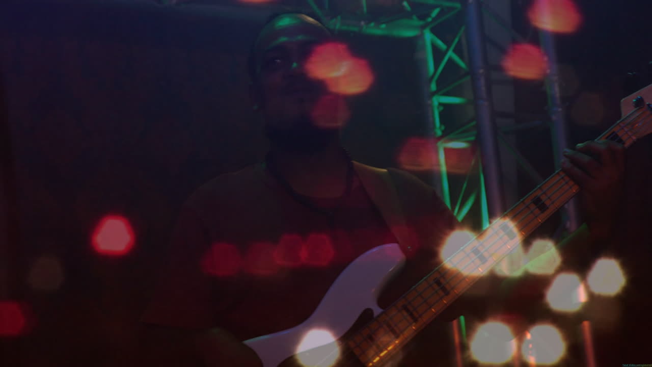 Musicista uomo che suona un basso bianco su un palco di un concerto musicale, che mostra sfere di luce bokeh animate