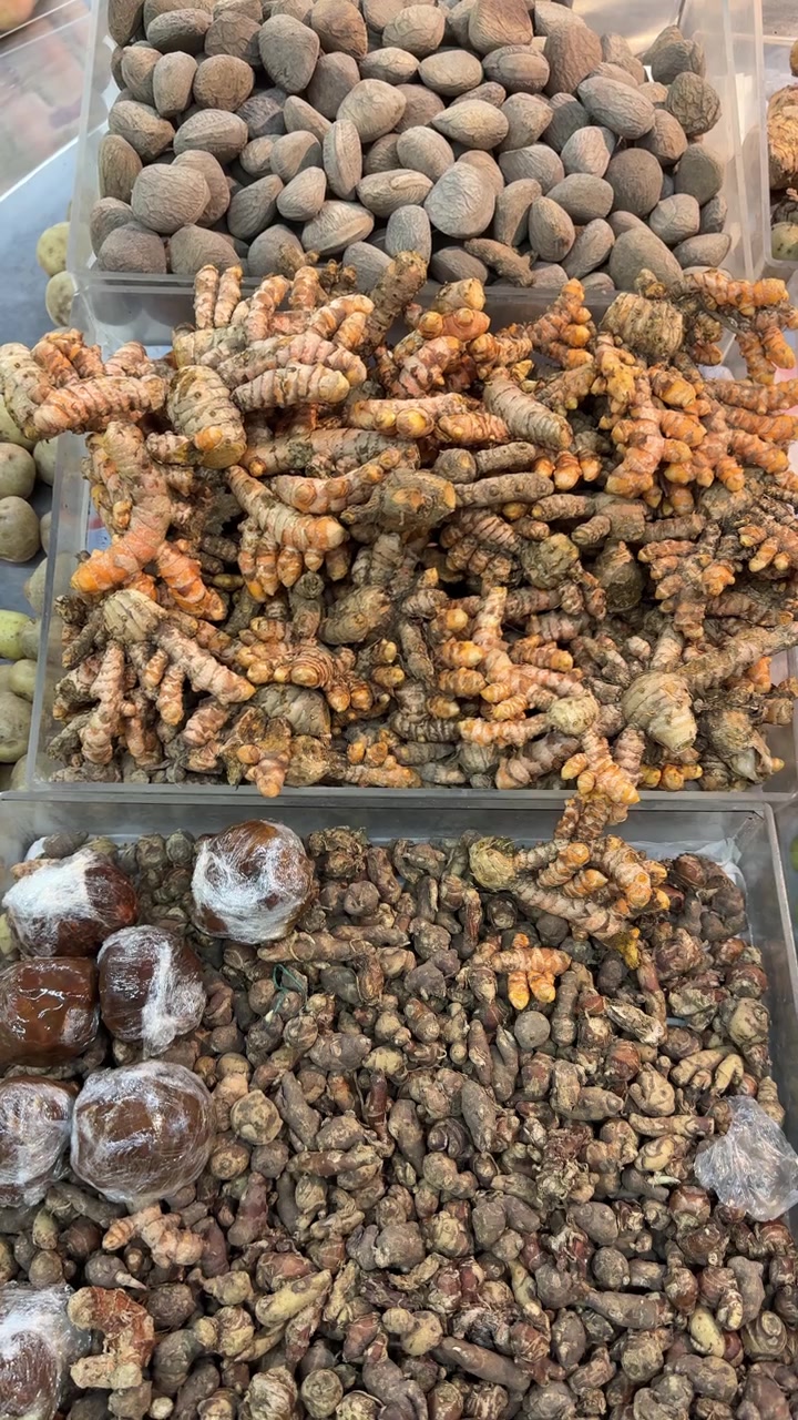 Свежие корни куркумы, имбирь и орехи, разложенные на рынке
