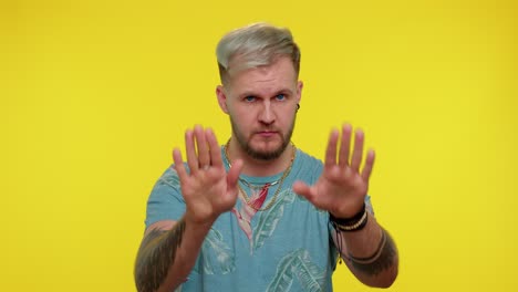 hombre con cabello rubio y barba con una camisa floral posa con las manos extendidas frente a un fondo amarillo