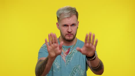 man with blonde hair and beard wearing a floral shirt poses with his hands outstretched in front of a yellow background