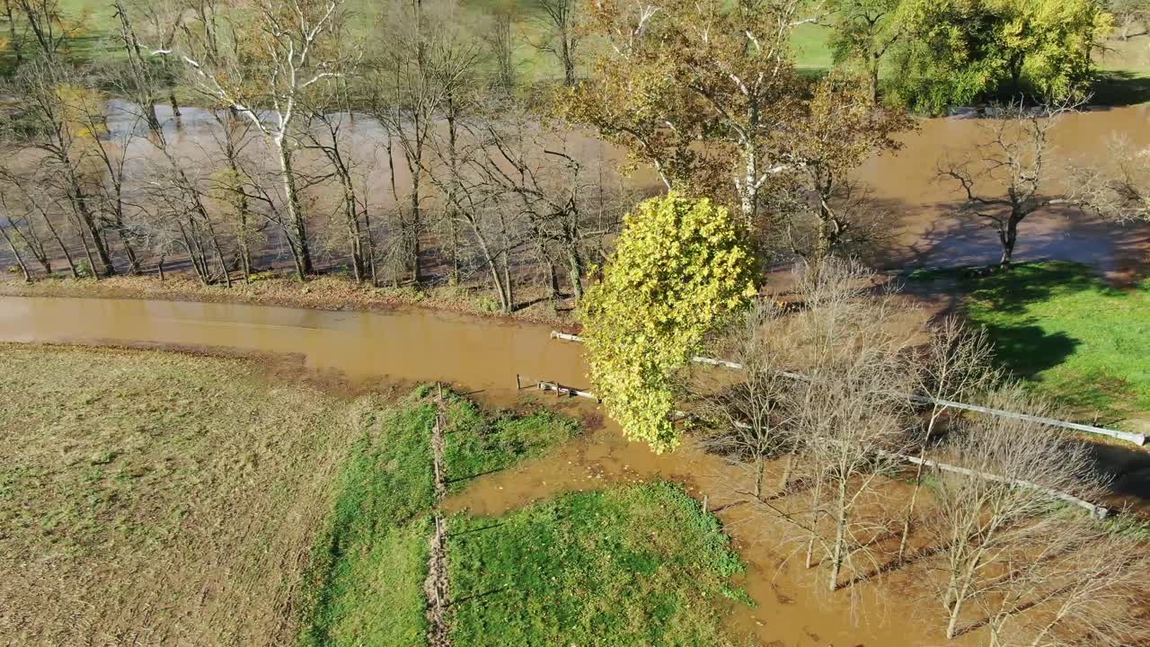 Aerial in autumn of flooded creek overflowing its banks into rural farm field on sunny day