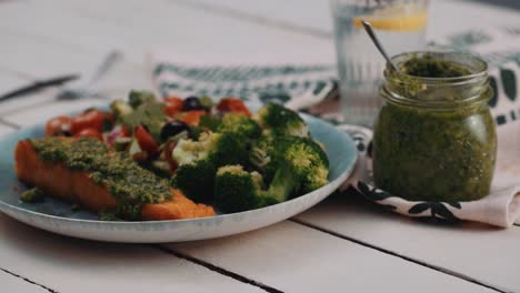 filete de salmón con salsa de pesto y verduras saludables servido en un plato redondo rústico sobre una mesa de madera
