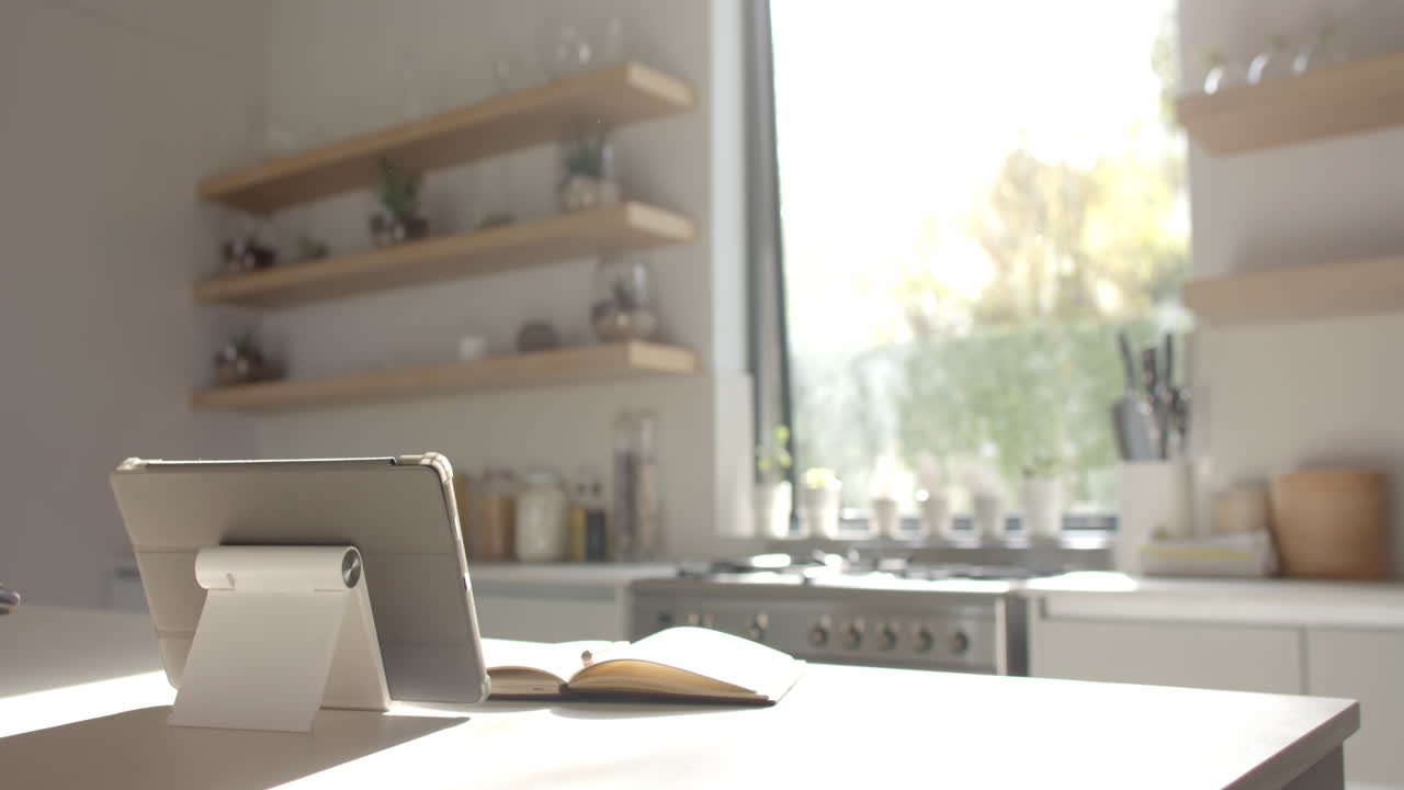 A tablet and notebook rest on kitchen counter, sunlight streaming in
