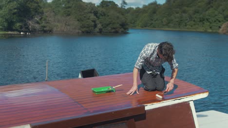 joven carpintero caucásico barnizando el techo de la cabina del barco de madera con rodillo