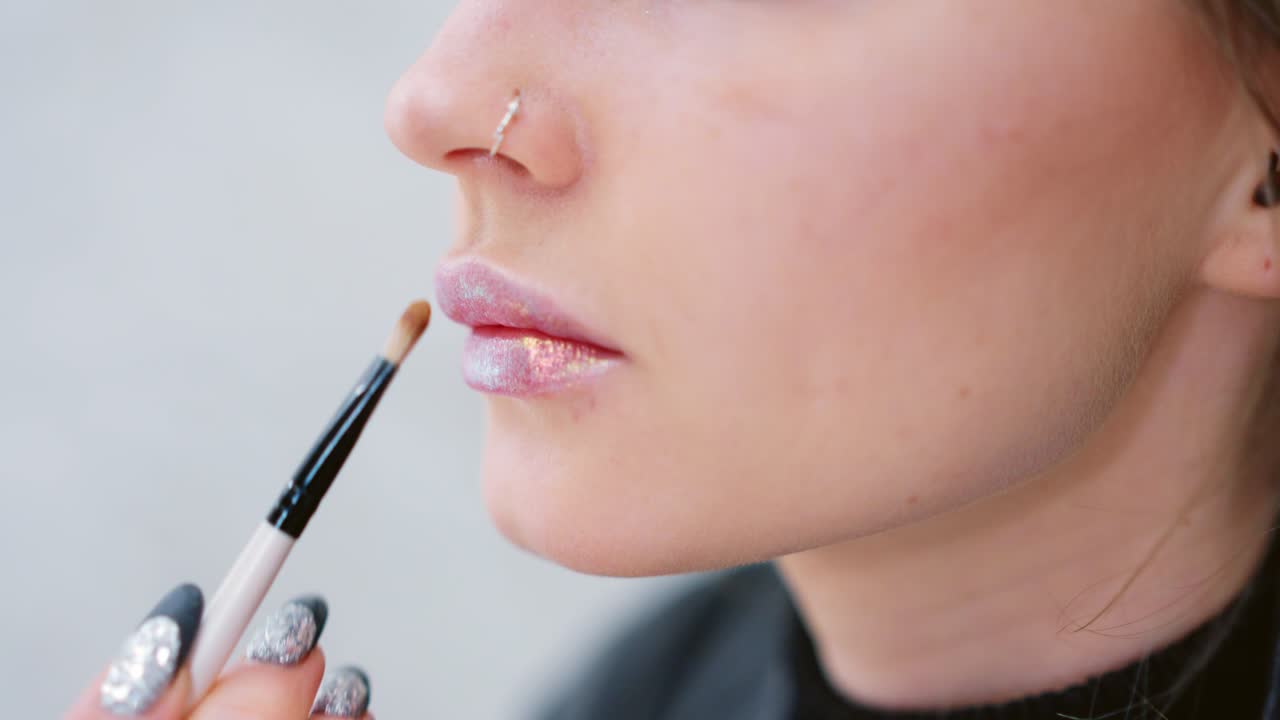 Close-up of a person applying glitter lip gloss with a brush