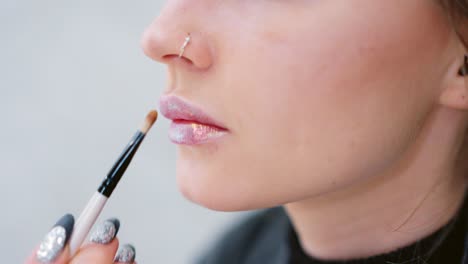 close-up of a person applying glitter lip gloss with a brush