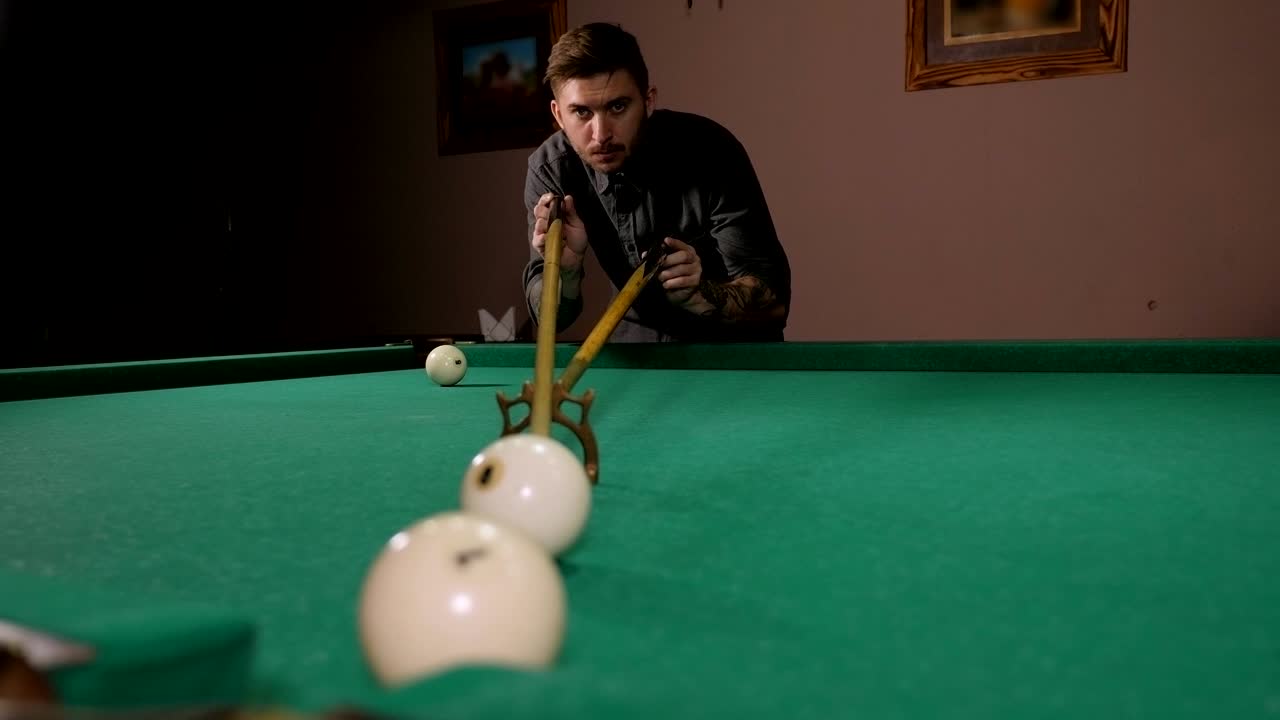Man met tatoeages op zijn handen speelt Russisch biljart in een donkere bar