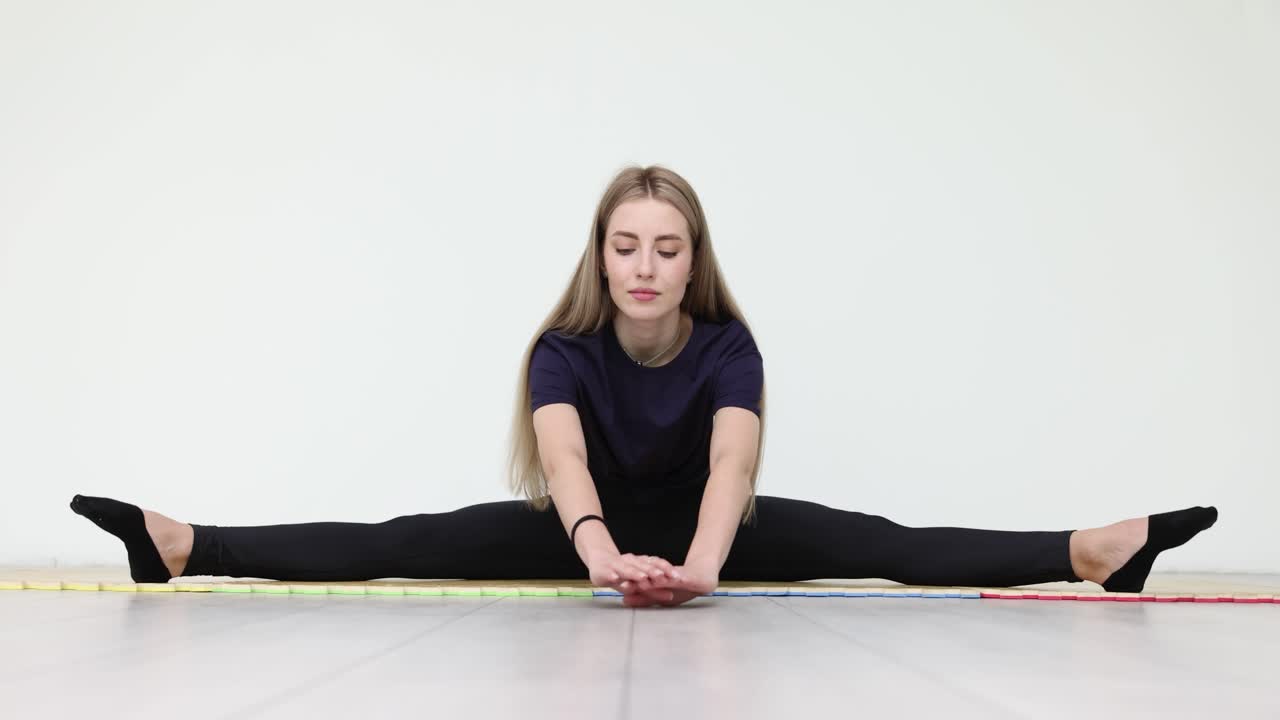 Donna in leggings e maglietta sportivi fa spaccate su tappetino da yoga