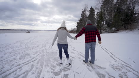 young couple ice skates in winter on frozen pond in maine