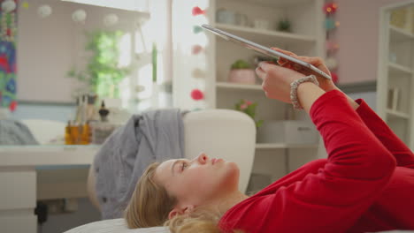 una adolescente con aparatos ortopédicos acostada en la cama en casa usando una tableta digital - filmada en cámara lenta