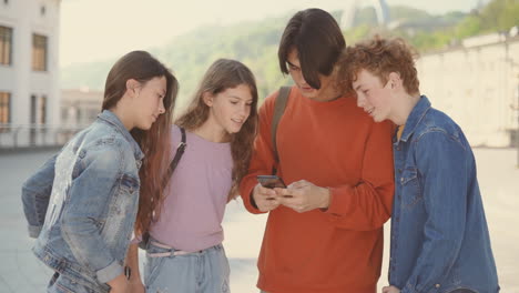 a group of teenagers with two girls and two boys watching something funny on a cell phone