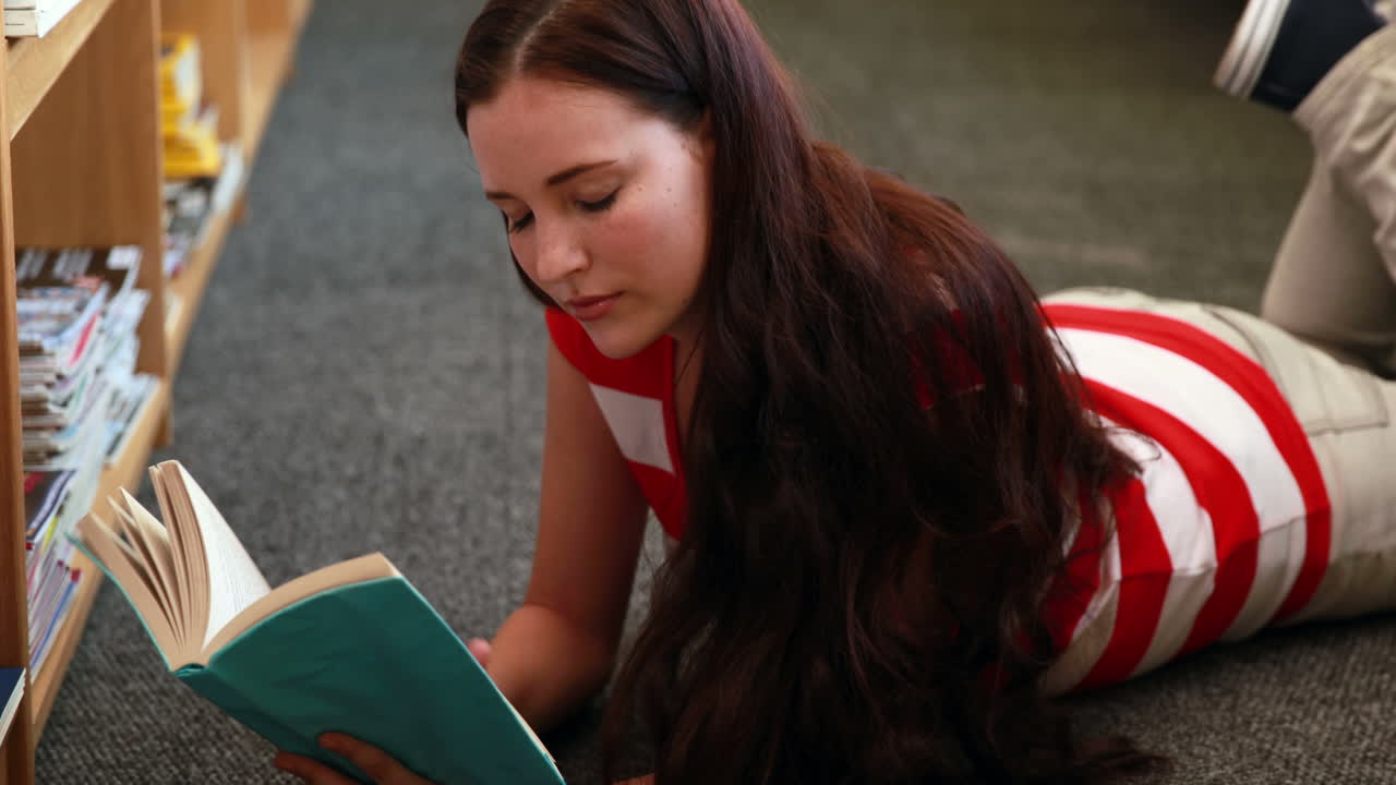 Bella studentessa che legge un libro sdraiata sul pavimento
