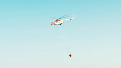 helicopter flying off after filling water bucket to drop on forest fire