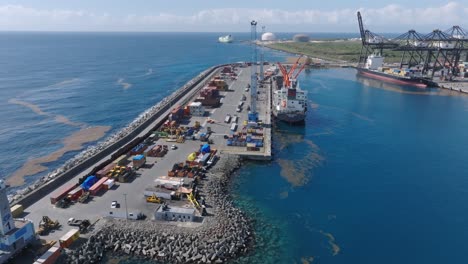 vuelo aéreo sobre el muelle en el puerto de caucedo con grúa y mercancías durante un día soleado - contaminación de petróleo en el mar caribe - contaminación ambiental en el puerto industrial