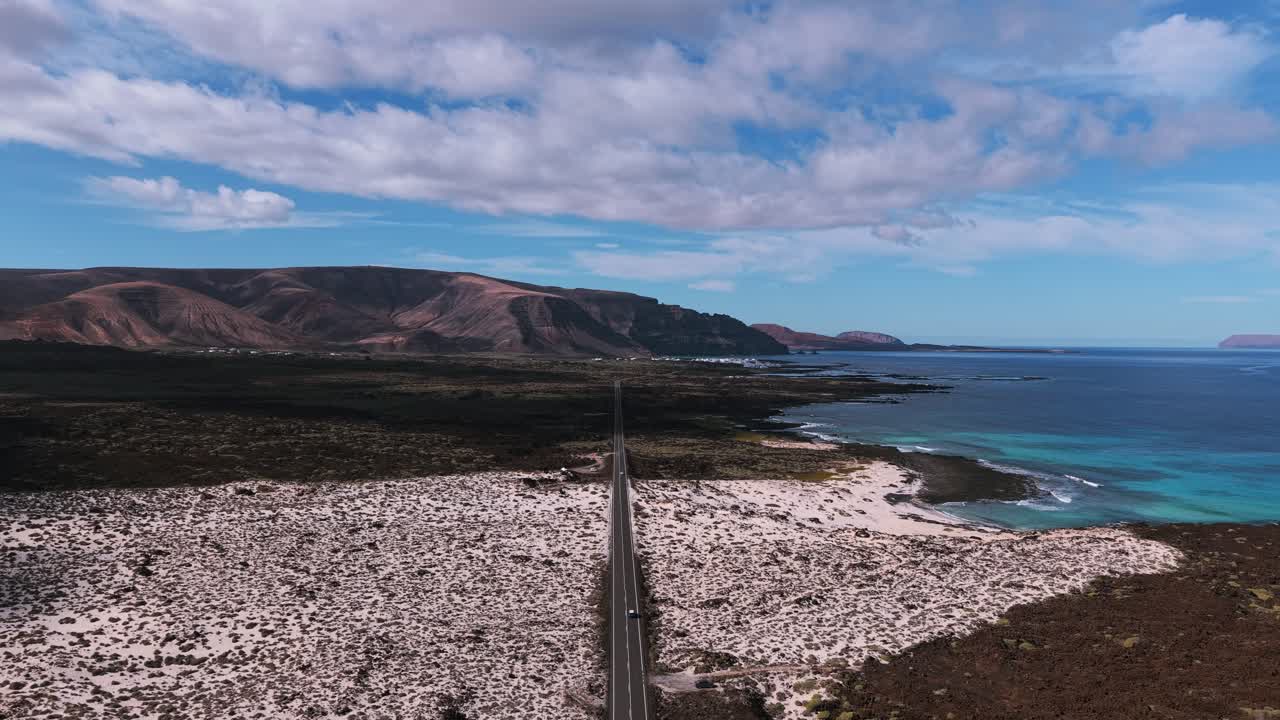 Luftfoto viser kystlinjen Caleton Blanco på Lanzarote, Kanariøyene, Spania, med turkist vann, svarte lavasteiner, hvit sand og en vei under en blå himmel. Dette er reiselivsturisme.