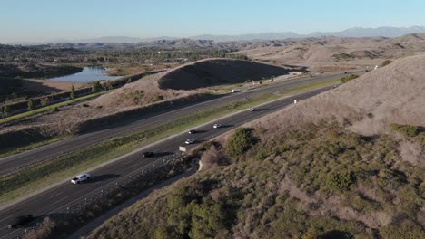 static shot of freeway with steady traffic, surrounded by trees with a lake in the distance