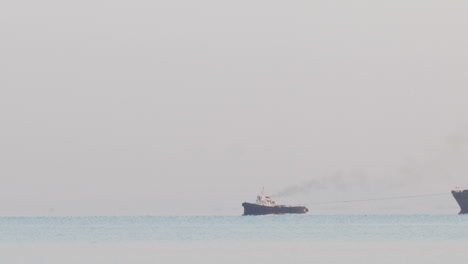 tugboat tugging a large barge in an overcast day