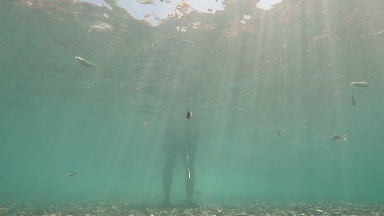 vista submarina del anzuelo de un pescador que pesca de pie en la orilla del mar mediterráneo