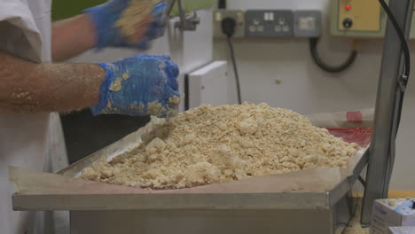 a worker add measures of crumble mix to a tray pf cake mix, removes some due to it being overweight