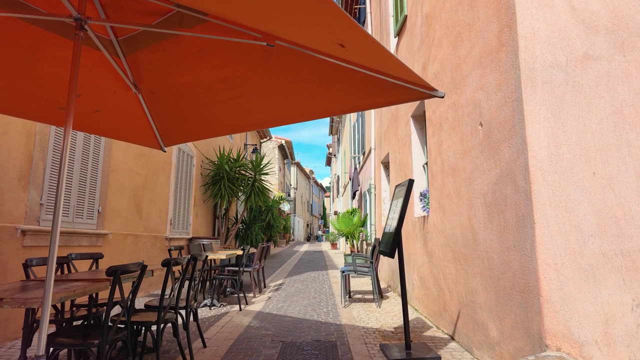 Un lento movimento di telecamera in avanti attraverso uno stretto vicolo francese con ombrelloni da caffè arancioni.