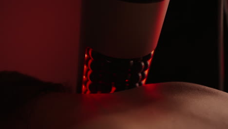 close-up of a massage therapist using a red light therapy device on a client's back