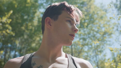 blurry moving trees and sunlight reflections on white man body in tank top adjusting white headband while scanning forest clearing under bright sun, sun flare dancing across bare skin