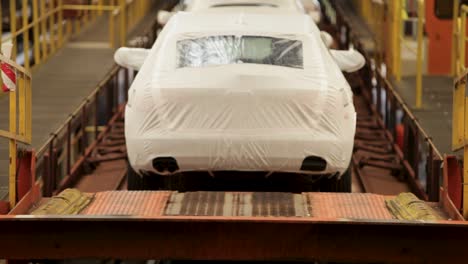 cars on an assembly line covered in protective white wraps, in an industrial setting, shallow focus