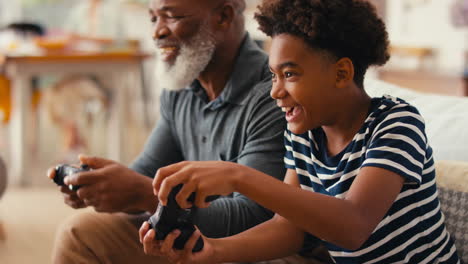 grandfather and grandson sitting on sofa at home playing video game together