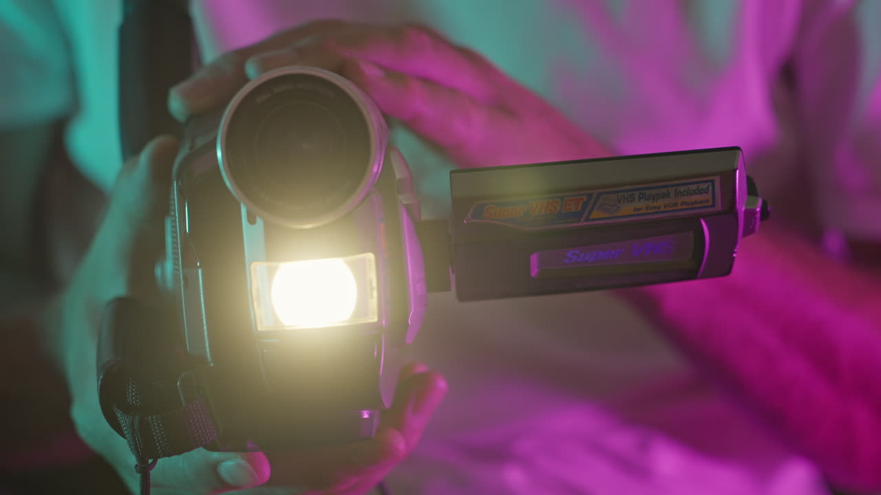 Hände halten Vintage-VHS-Camcorder mit leuchtendem Licht und Neonhintergrund