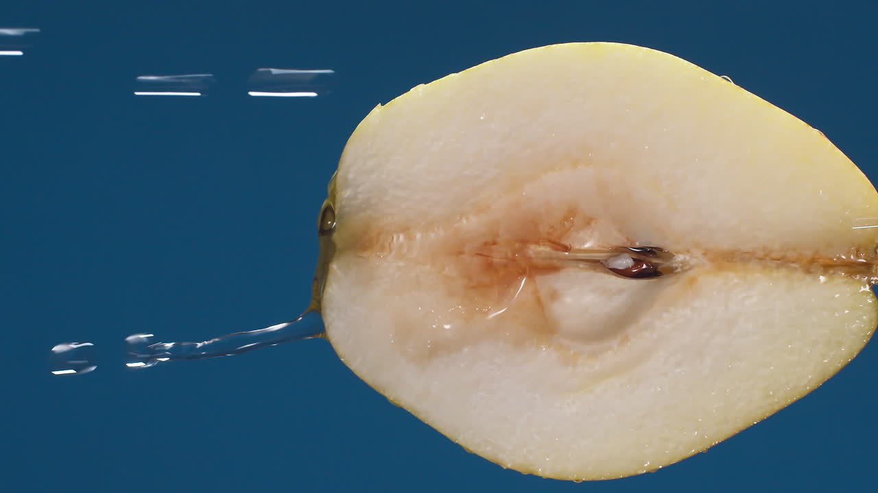 media pera amarilla vertical sobre un fondo azul oscuro con gotas de agua rodando por la pera y salpicando con un fondo aislado