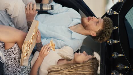 video vertical: una chica rubia le da a su novio barbudo con cabello rizado en una camisa azul un sabor de pizza, después de lo cual él