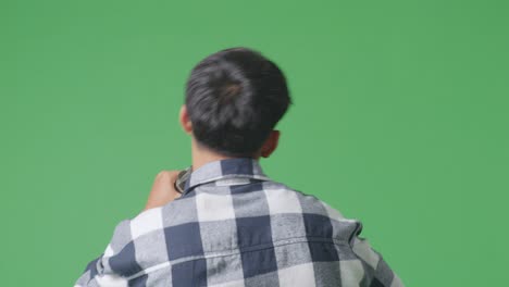 close up back view of young asian teen boy holding a microphone and rapping on the the green screen background