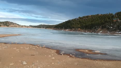 aerial push in of frozen lake with thick ice and mountains in colorado mountain town