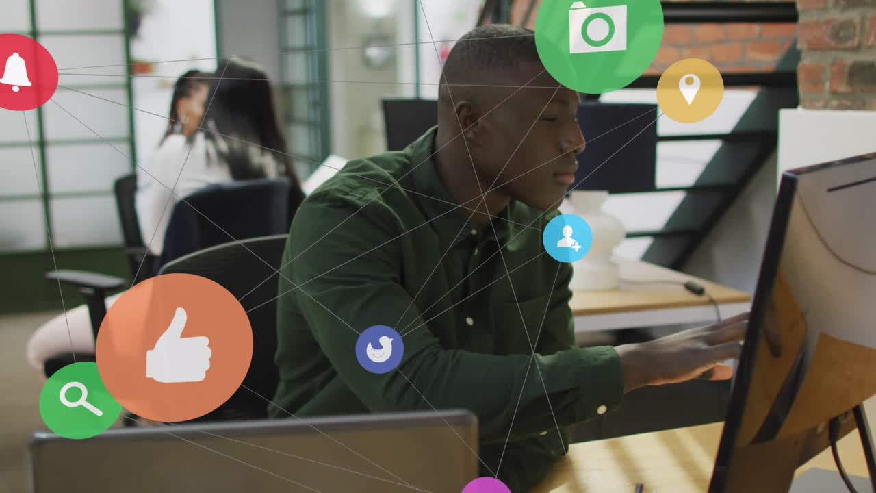 Animation of network of digital icons over african american man using computer and laptop at office